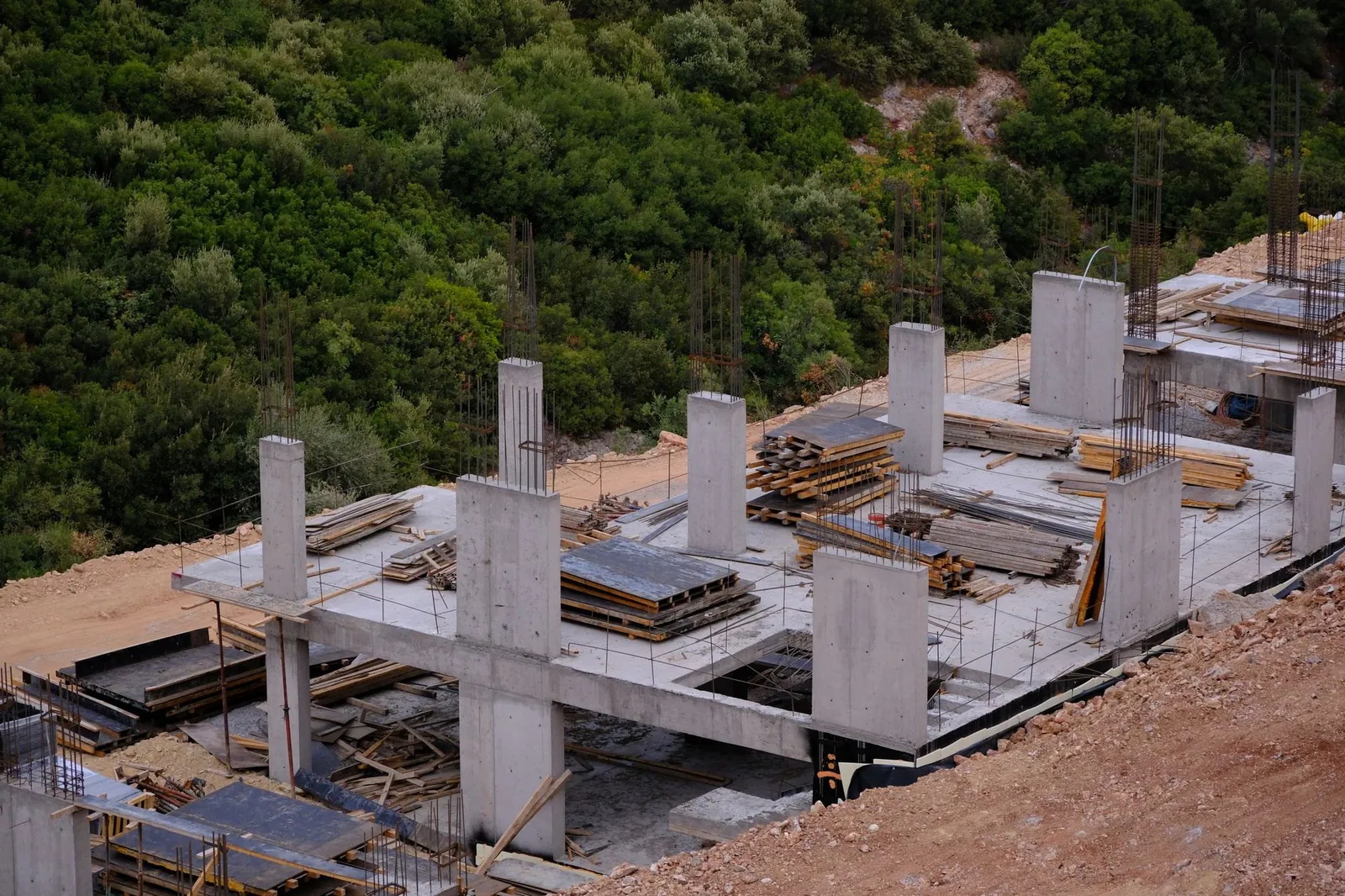 A concrete frame and slab going up on a forested hillside, from the air