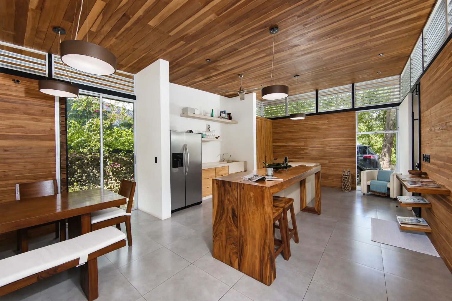 Kitchen and dining room under a timber ceiling, with a solid wood island and high louvred windows