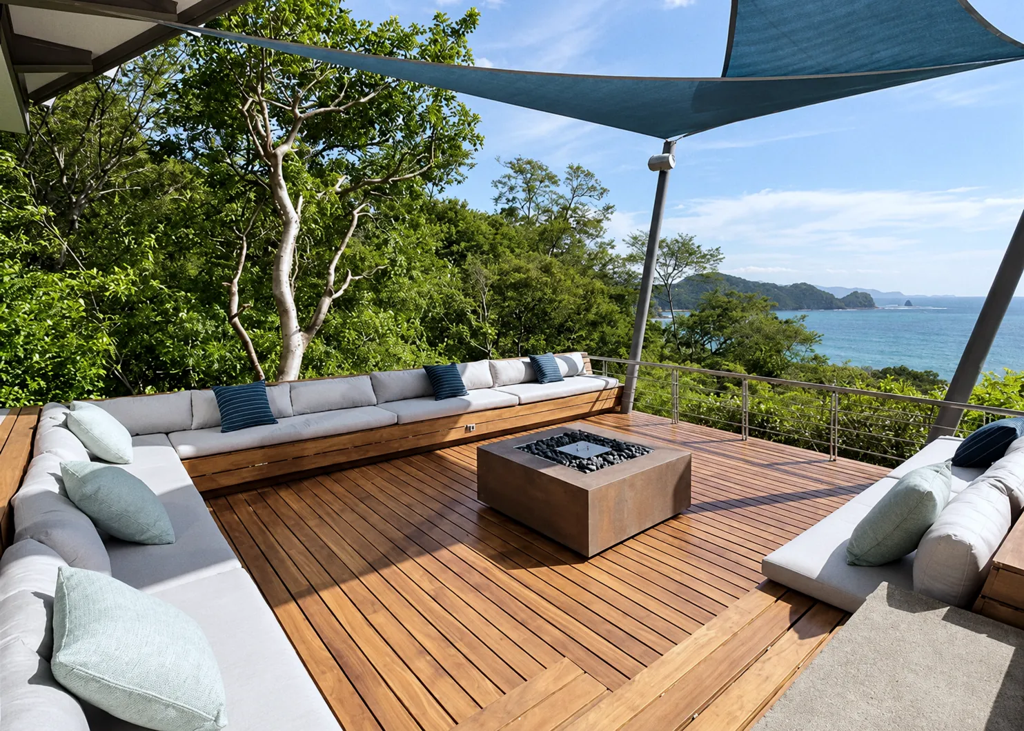 Sunken lounge with built-in sofas and a fire pit under a shade sail, looking out to the bay